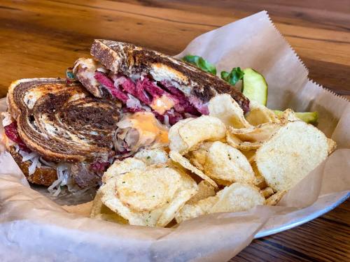 A hearty sandwich with layers of meat and cheese, served with a side of crispy potato chips and pickles.