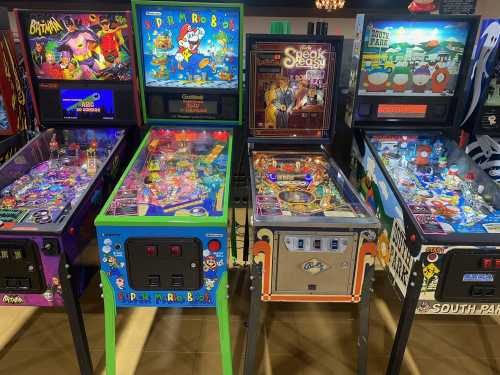 A row of colorful pinball machines featuring various themes, including cartoons and games, in a vibrant arcade setting.