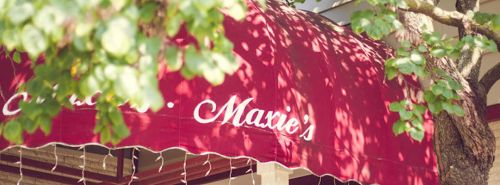 A red awning with the name "Marie's" partially visible, surrounded by green leaves and soft sunlight.