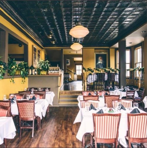 Elegant restaurant interior with wooden floors, white tablecloths, and greenery, featuring a warm color palette and vintage decor.