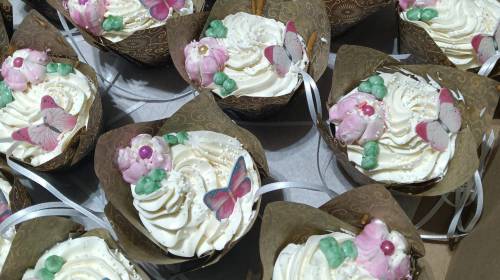 Decorative cupcakes with swirls of frosting, topped with edible flowers and butterflies in elegant wrappers.