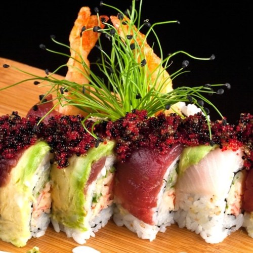 A colorful sushi platter featuring various rolls topped with fish, avocado, and caviar, garnished with crispy shrimp and herbs.
