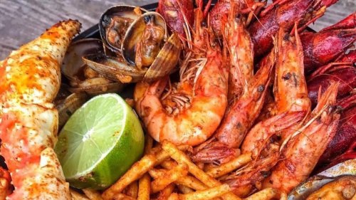 A close-up of a seafood platter featuring shrimp, crab, clams, and a lime wedge, garnished with spices and fries.