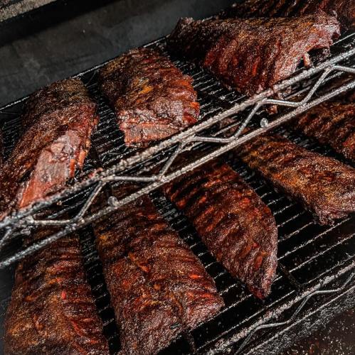 Close-up of smoked ribs on a grill, showcasing a rich, dark bark and juicy texture.