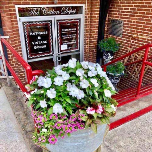 A flower planter with white and pink blooms in front of The Cotton Depot, an antiques and vintage goods store.