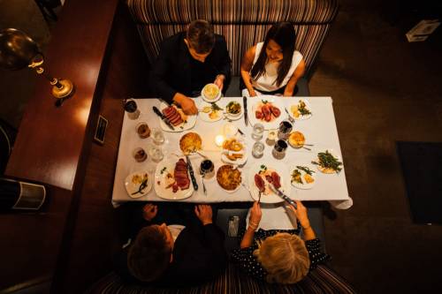 Aerial view of four people dining at a table with various dishes and drinks in a cozy restaurant setting.
