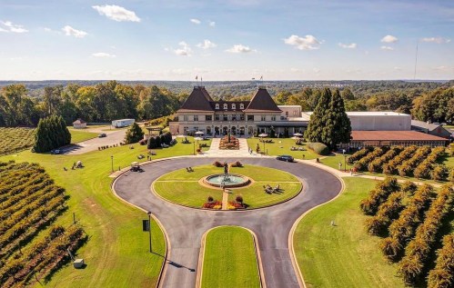 Aerial view of a grand building surrounded by landscaped gardens and a circular driveway with a fountain.