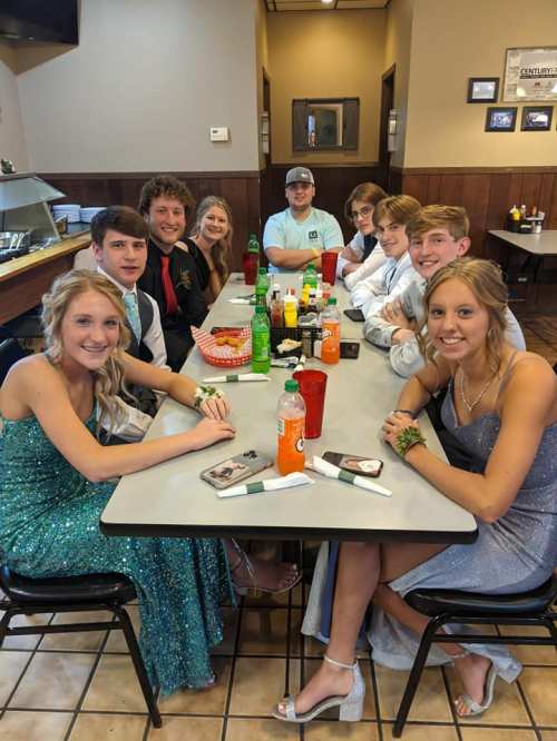 A group of ten young people in formal attire sitting at a table with drinks and food in a restaurant.