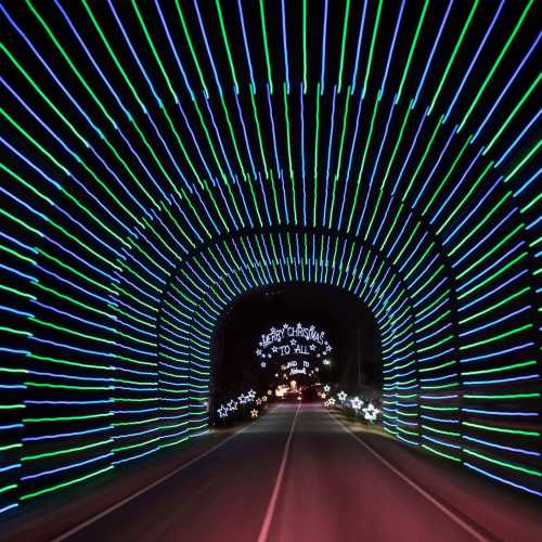 A brightly lit tunnel of green and blue lights with a "Merry Christmas to All" sign at the end.