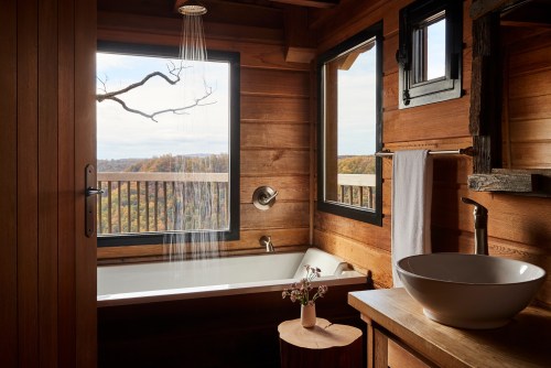 Cozy wooden bathroom with a shower, bathtub, and large windows showcasing a scenic outdoor view.