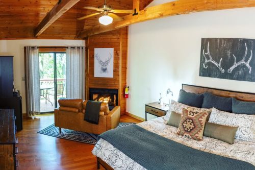 Cozy bedroom with wooden beams, a fireplace, and a balcony view, featuring a large bed and rustic decor.