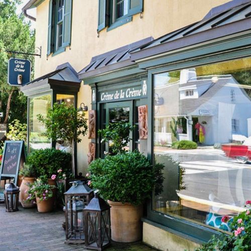 Charming storefront with plants, lanterns, and a sign for "Crème de la Crème" on a sunny day.