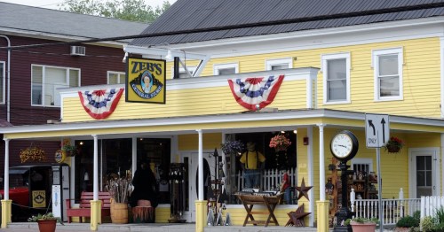 A bright yellow storefront with patriotic decorations and a clock outside, featuring various items for sale.
