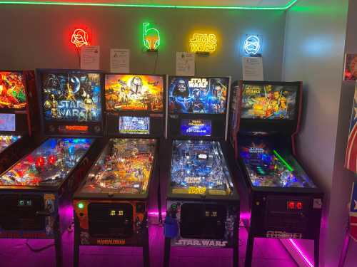 A row of Star Wars-themed pinball machines with colorful neon lights in a game room.