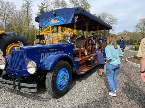A vintage blue truck with a wooden seating area, surrounded by people enjoying a sunny day outdoors.