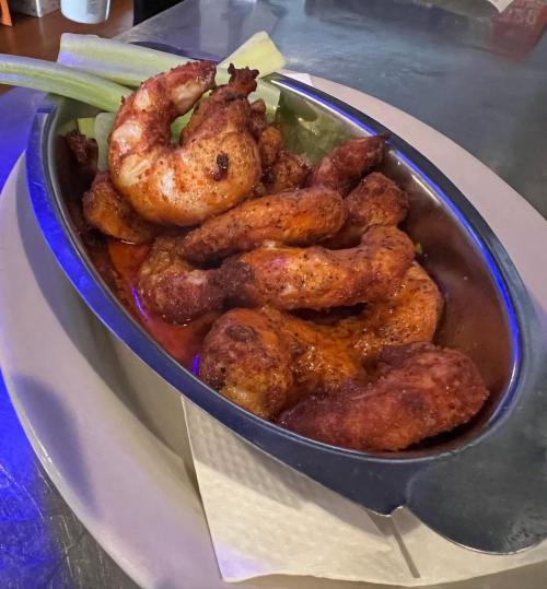 A metal dish filled with crispy fried shrimp, garnished with celery, resting on a plate.