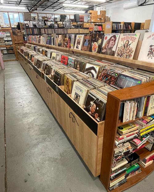 A spacious record store with wooden shelves filled with vinyl records and albums, organized neatly in a well-lit area.