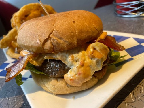A close-up of a juicy burger with bacon, lettuce, and sauce, served on a plate with a toothpick.