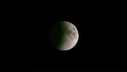 A partially illuminated moon against a black sky, showcasing a shadowed hemisphere.