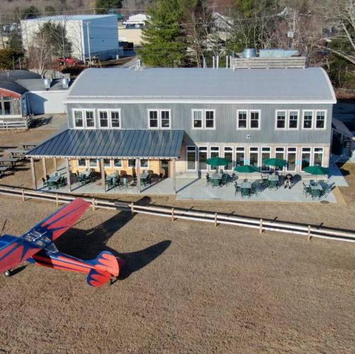 Aerial view of a modern building with outdoor seating and a vintage biplane in a grassy area.