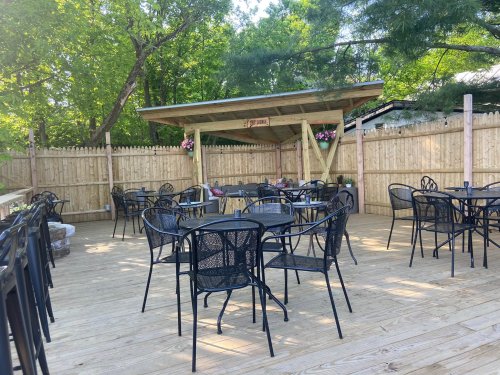 Outdoor seating area with black metal tables and chairs, surrounded by a wooden fence and greenery.