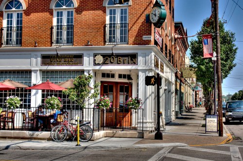 A charming restaurant with outdoor seating, flower planters, and a bicycle parked outside on a sunny street.