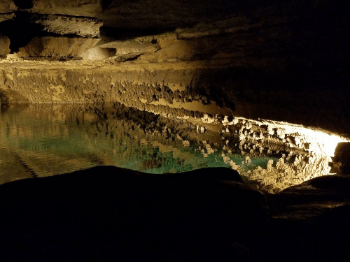 A dark cave interior with a calm, reflective pool of water illuminated by soft light.
