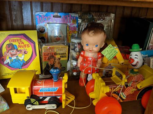 A shelf filled with vintage toys, including a doll, a clown figure, and colorful toy vehicles.