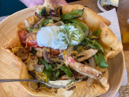 A crispy tortilla bowl filled with grilled chicken, sautéed peppers, cheese, guacamole, and sour cream.