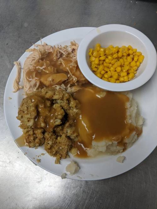 A plate of food featuring shredded chicken, stuffing, mashed potatoes with gravy, and a side of corn.