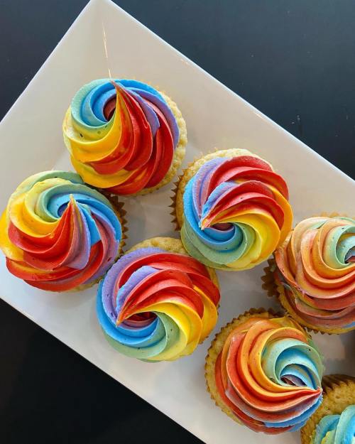 A platter of colorful cupcakes with swirled rainbow frosting in vibrant shades of red, blue, yellow, and green.