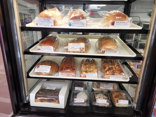 A display case filled with various types of bread and pastries, all neatly packaged and labeled.