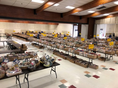 A spacious room filled with tables stacked with books and baskets, set up for a book sale event.