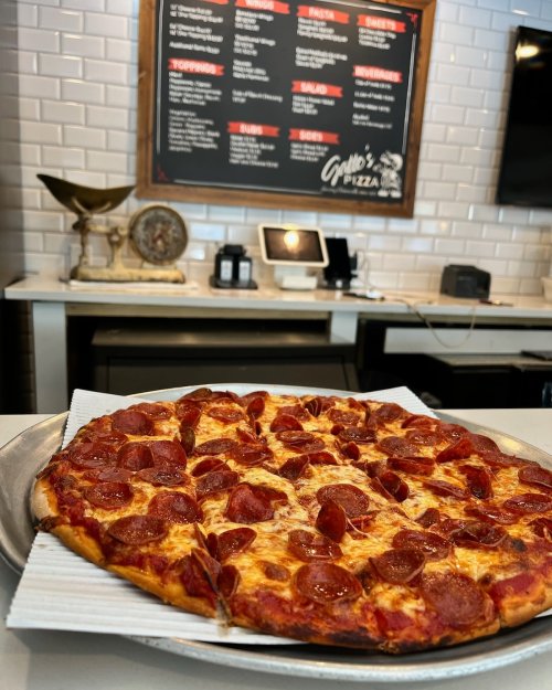 A freshly baked pepperoni pizza on a silver platter, with a menu board in the background.