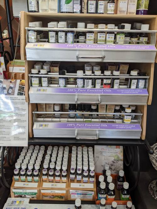 A display of various essential oils in bottles, organized on shelves with labels indicating "100% Pure Essential Oils."
