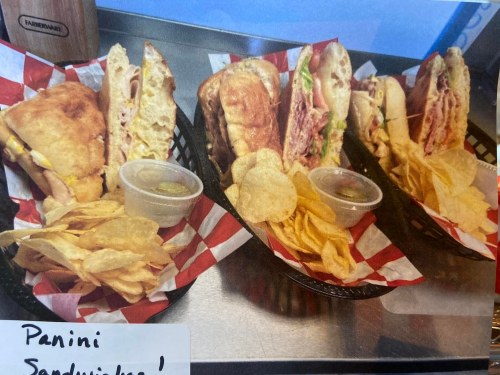 Three baskets of panini sandwiches with chips on the side, featuring red and white checkered liners.