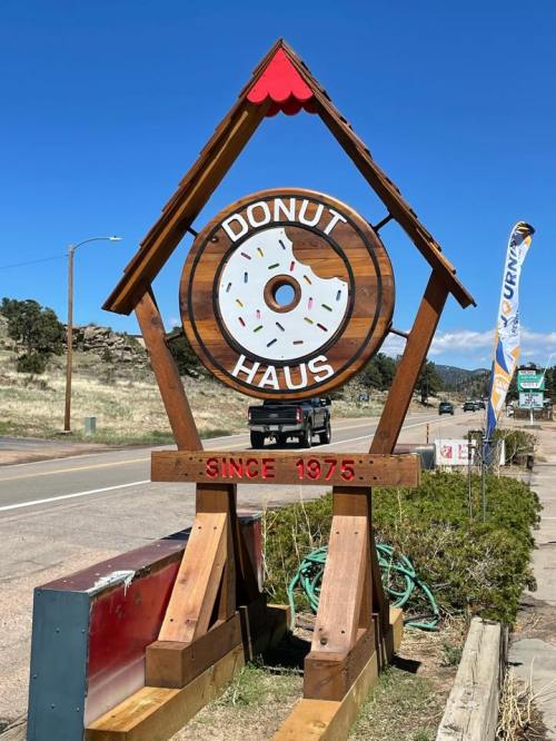 Sign for "Donut Haus" featuring a donut graphic, established in 1975, set against a clear blue sky.
