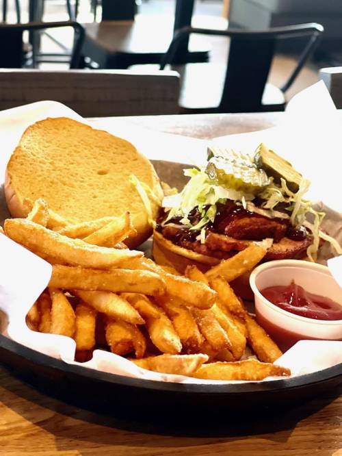 A plate with a sandwich topped with pickles and lettuce, served with crispy fries and a side of ketchup.