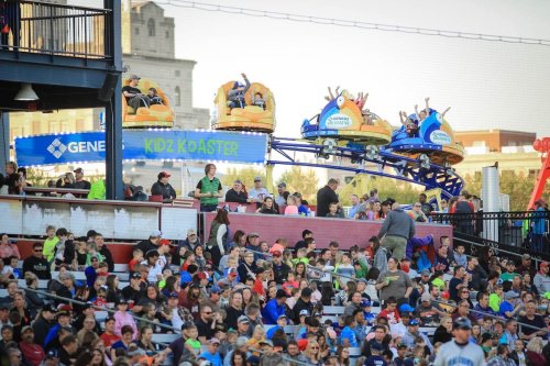A crowded amusement park with a roller coaster named "Kidz Koaster" in the background and excited riders on the ride.