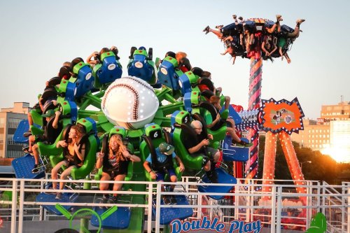 A vibrant amusement park scene with two thrilling rides and excited riders enjoying the attractions at sunset.