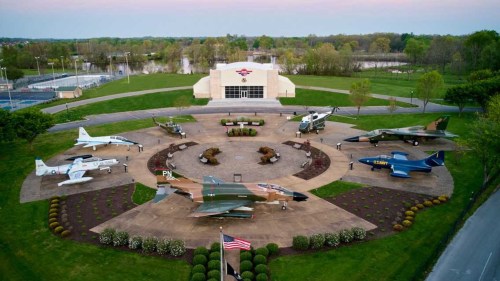 Aerial view of a military aircraft display with various planes arranged around a central building and landscaped grounds.