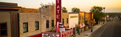 A vintage movie theater marquee stands prominently on a charming street lined with shops at sunset.