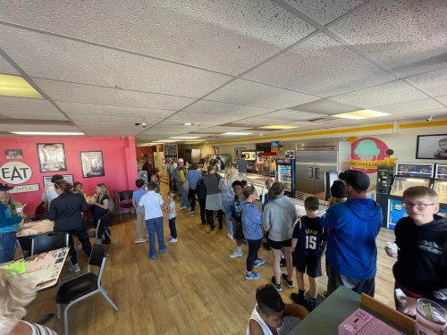 A busy ice cream shop with customers lining up at the counter and seating areas filled with people.