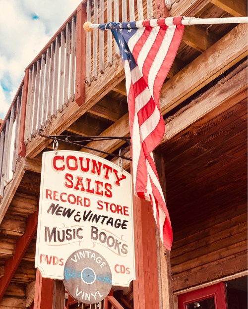 Sign for "County Sales Record Store" featuring vintage music, books, and DVDs, with an American flag hanging nearby.