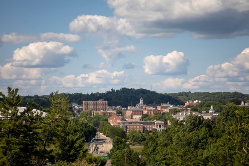 A scenic view of a town with buildings and trees, set against a backdrop of blue sky and fluffy clouds.
