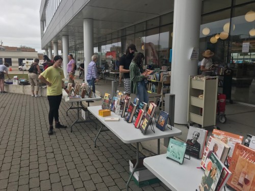 A book sale outside a building, with tables displaying various books and people browsing.