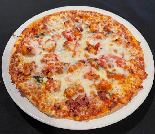 A freshly baked pizza topped with melted cheese, chunks of meat, and vegetables on a white plate.