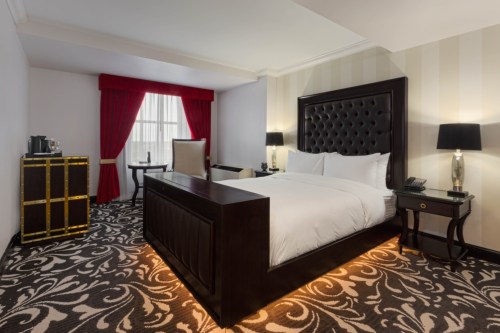 A stylish hotel room featuring a large bed, elegant decor, a desk, and red curtains by a window.