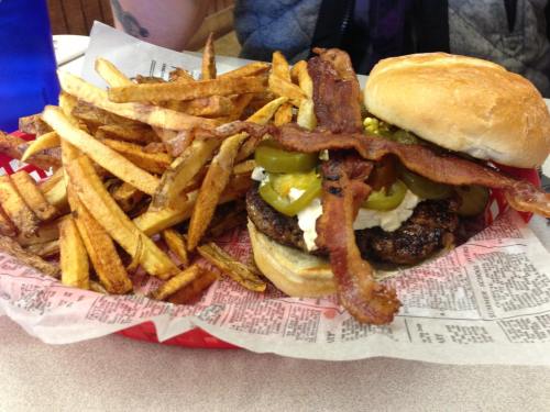 A hearty burger topped with bacon and jalapeños, served with a side of crispy fries in a red basket.