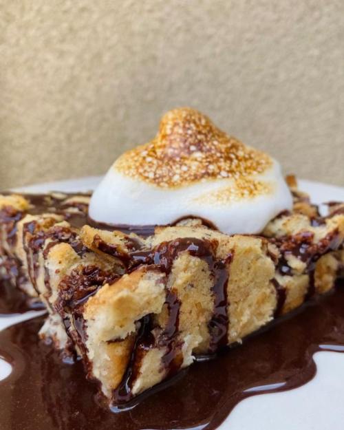 A slice of dessert drizzled with chocolate sauce, topped with a toasted meringue swirl on a white plate.